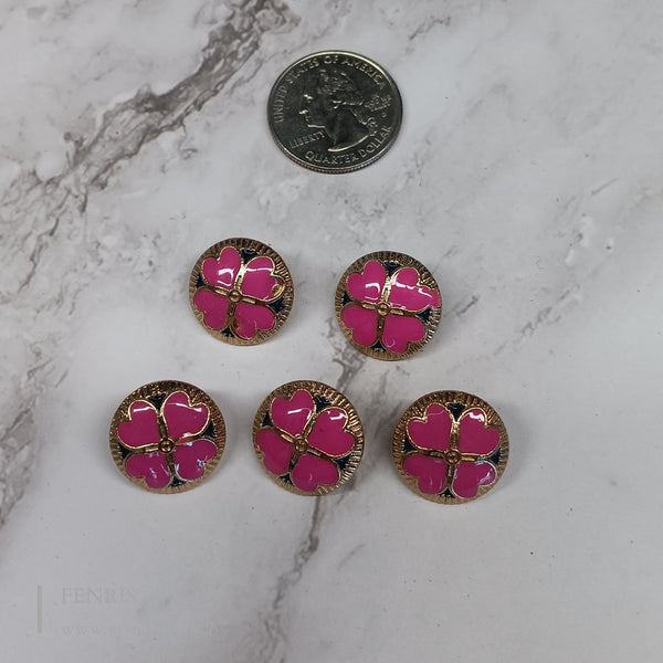 Five pink floral buttons with gold accents on a marble surface next to a coin for scale.